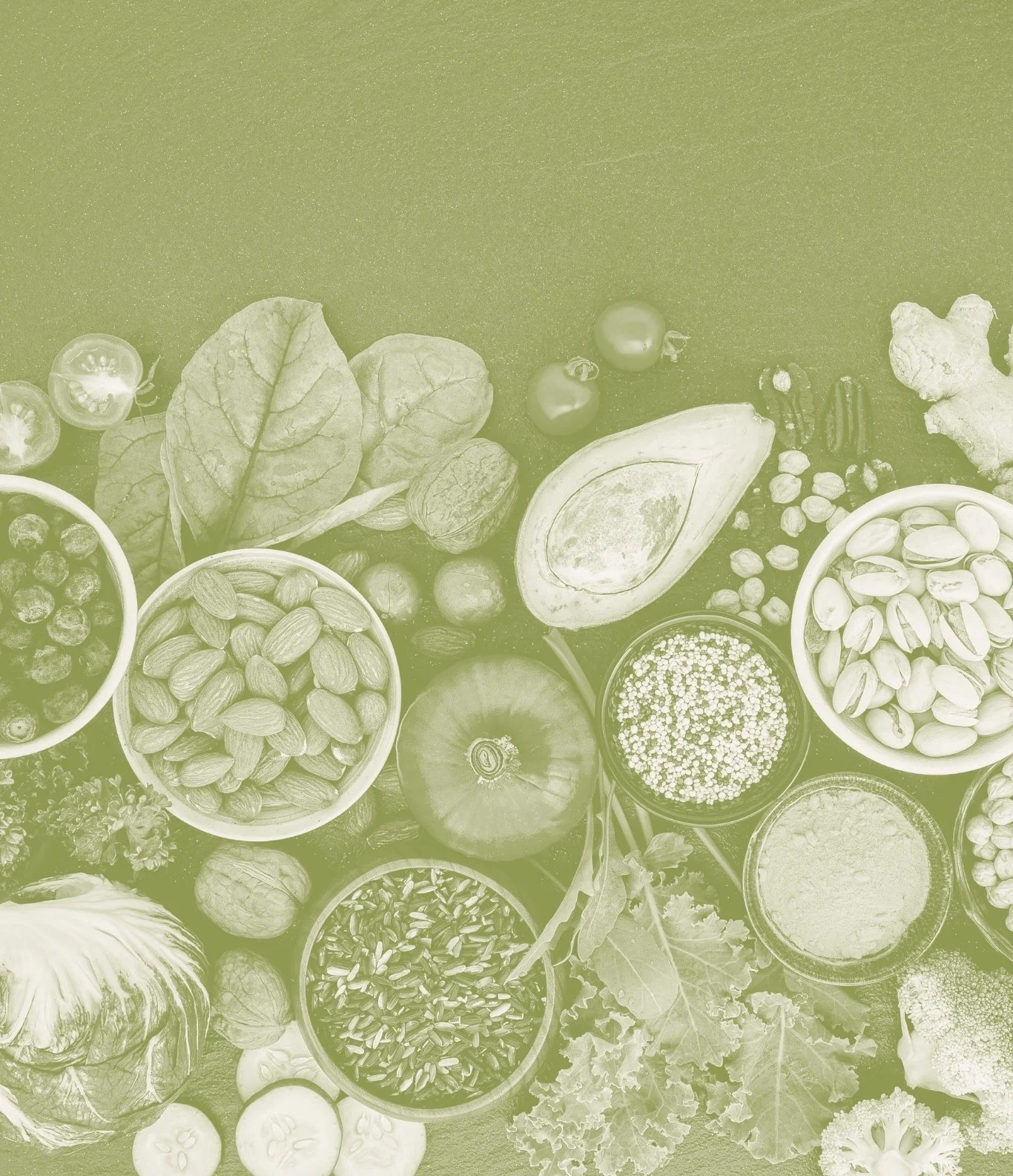 Various fresh vegetables, fruits, nuts, and seeds arranged on a table, including cherry tomatoes, spinach, walnuts, avocado, ginger, pistachios, chickpeas, an apple, cauliflower, and lettuce.