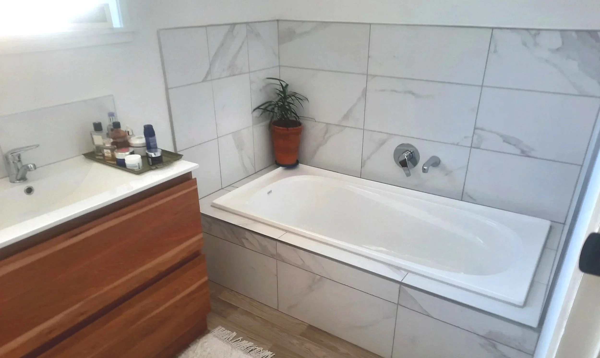 A bathroom with a corner bathtub, a potted plant, a sink with various toiletries, and a wooden cabinet.