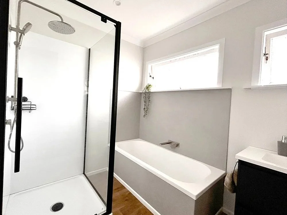 Modern bathroom with a walk-in shower, a bathtub beneath a window, and a small vanity with a sink.
