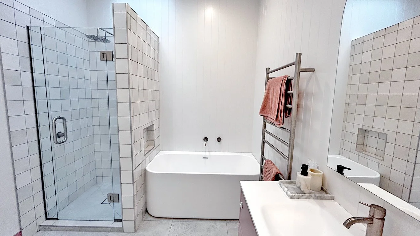 Modern bathroom with a glass-enclosed shower, white bathtub, towel rack, and a sink with toiletries.