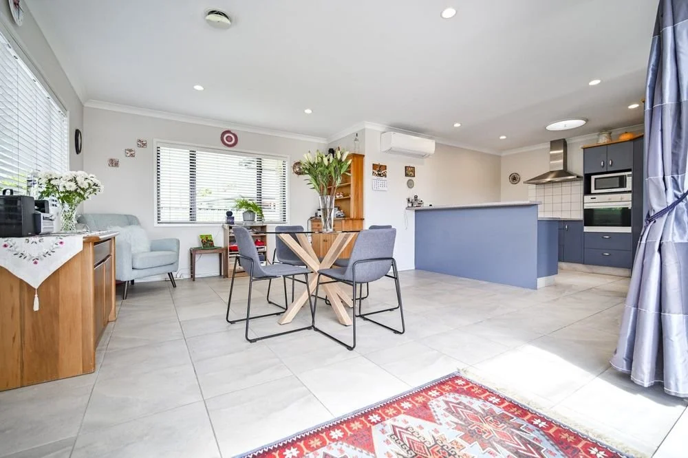 Open kitchen and living room with dining table, chairs, armchair, bookshelf, and large windows in a bright, modern home.
