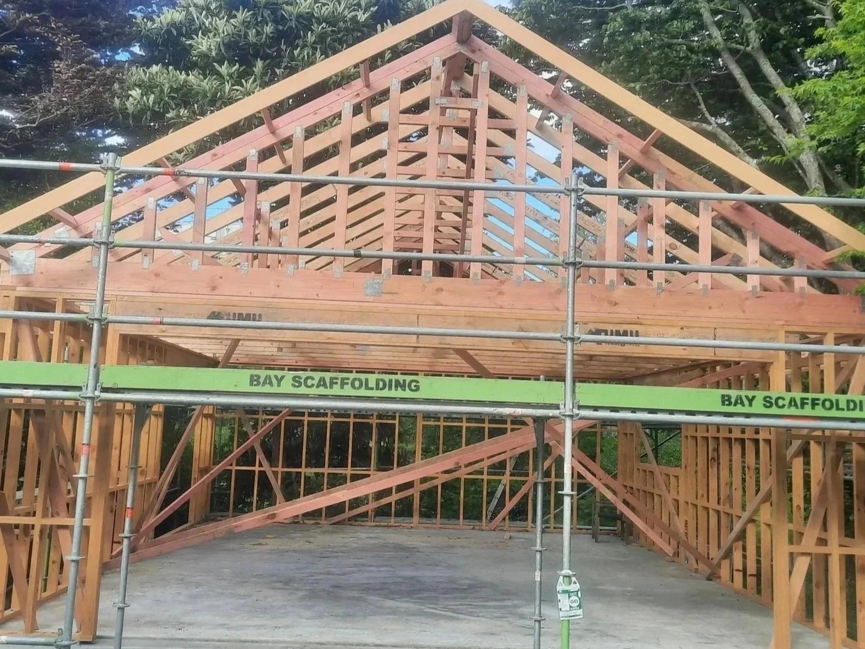 Wooden framing of a house under construction with scaffolding labeled 'BAY SCAFFOLDING' in front.