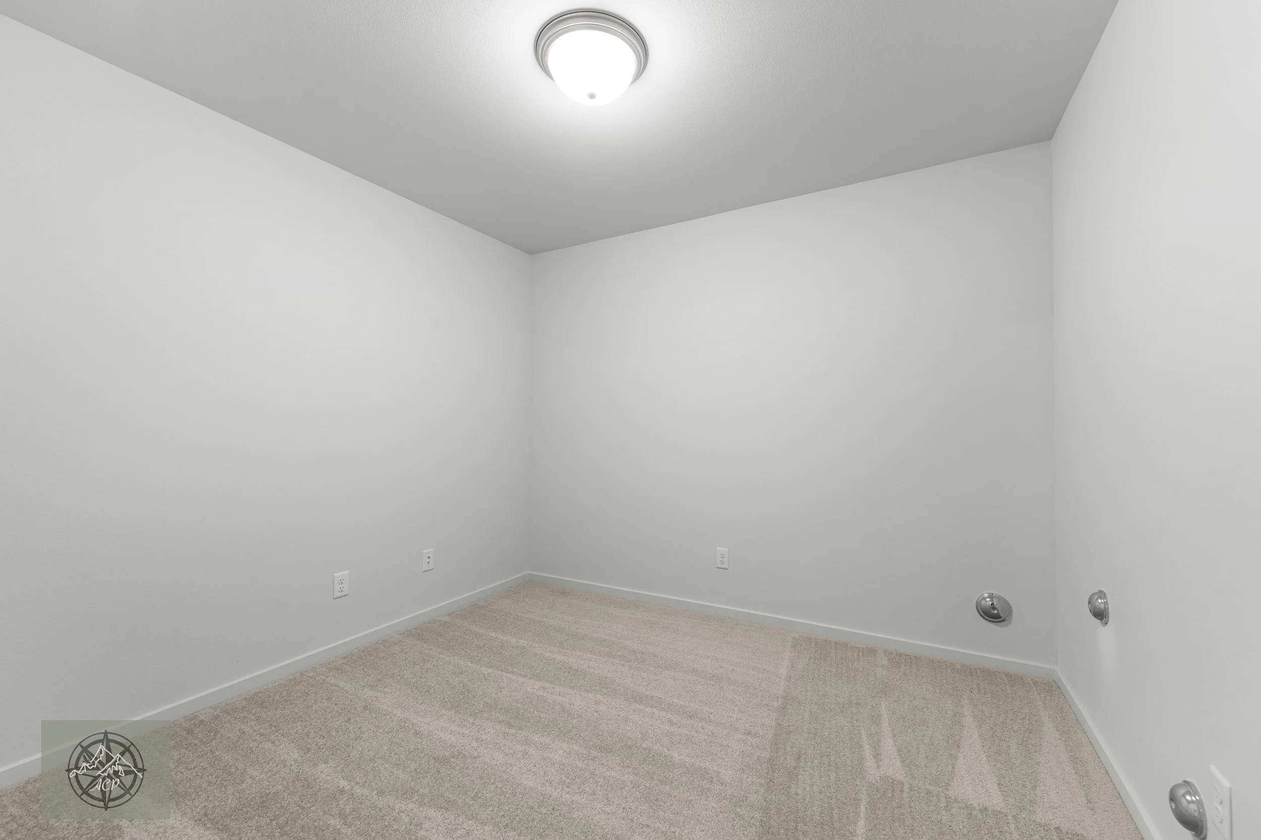 Empty white room with beige carpet, four electrical outlets, and a ceiling light fixture.