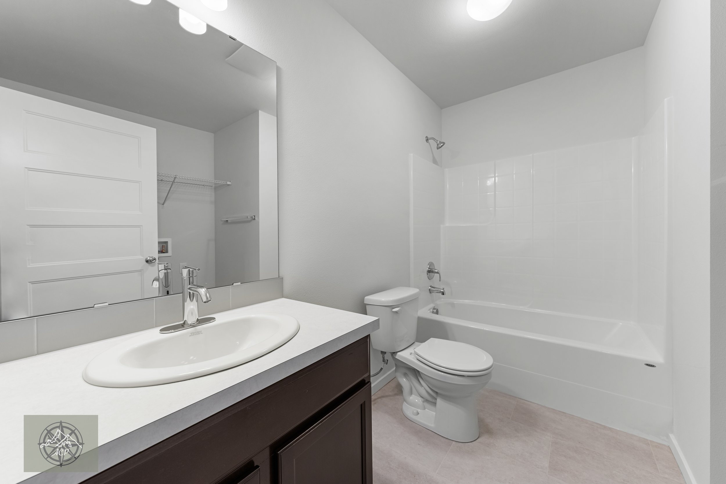 Empty bathroom with a white bathtub and shower, a toilet, a sink with a dark cabinet, and a large mirror.