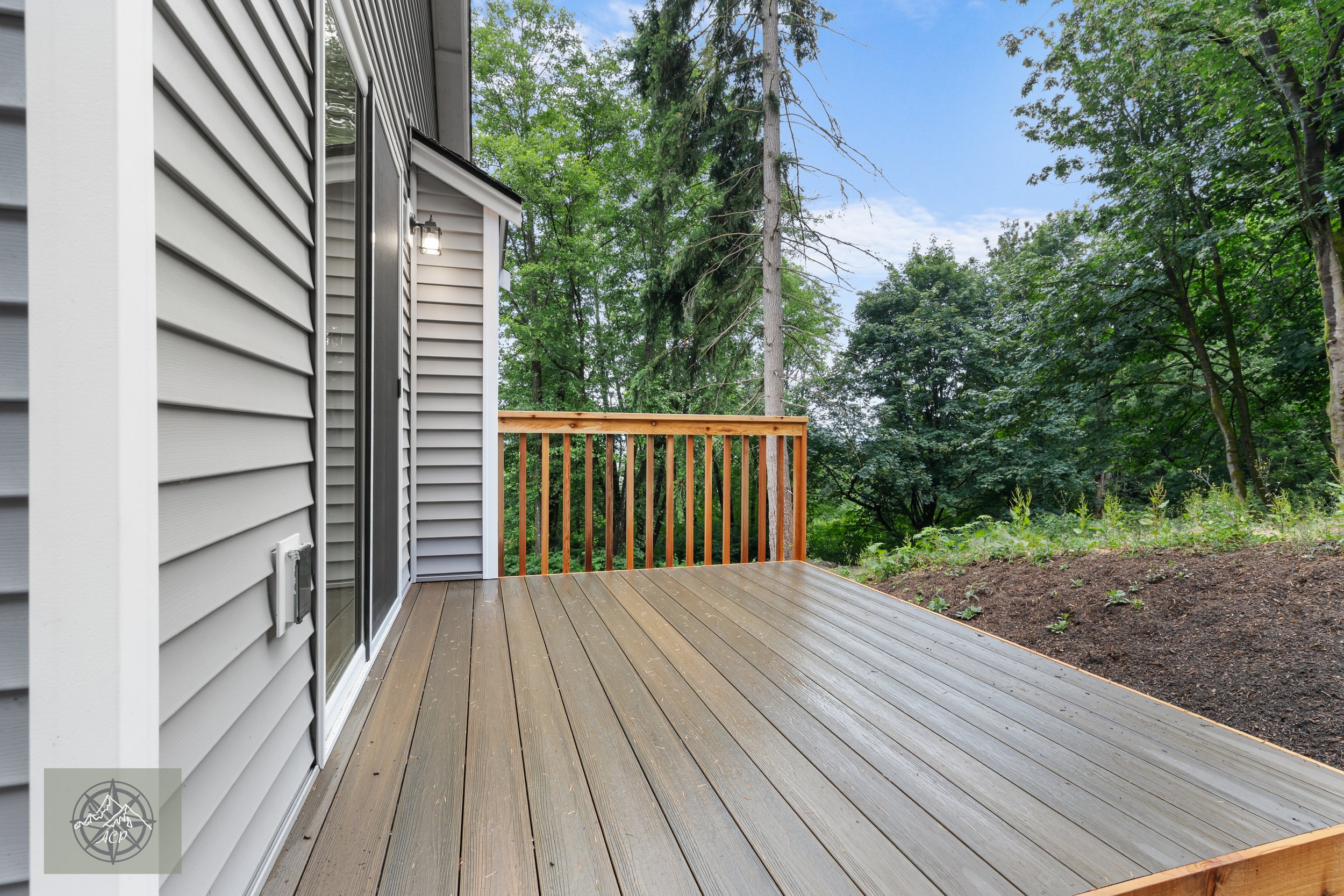 Wooden deck attached to a house with vinyl siding, overlooking a wooded yard with trees and green foliage.