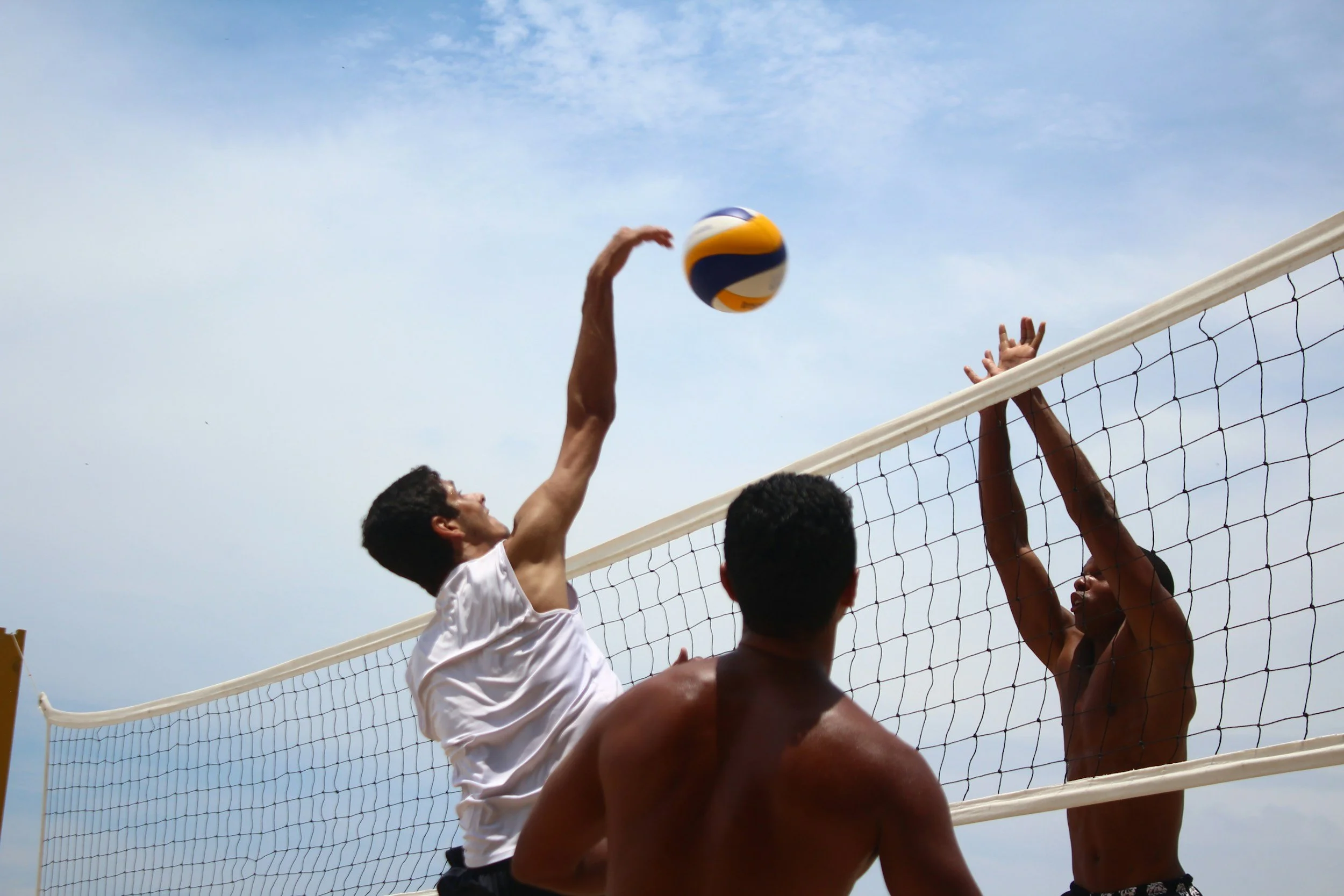 Beach volleyball player jumping to spike the ball over the net on a sand court