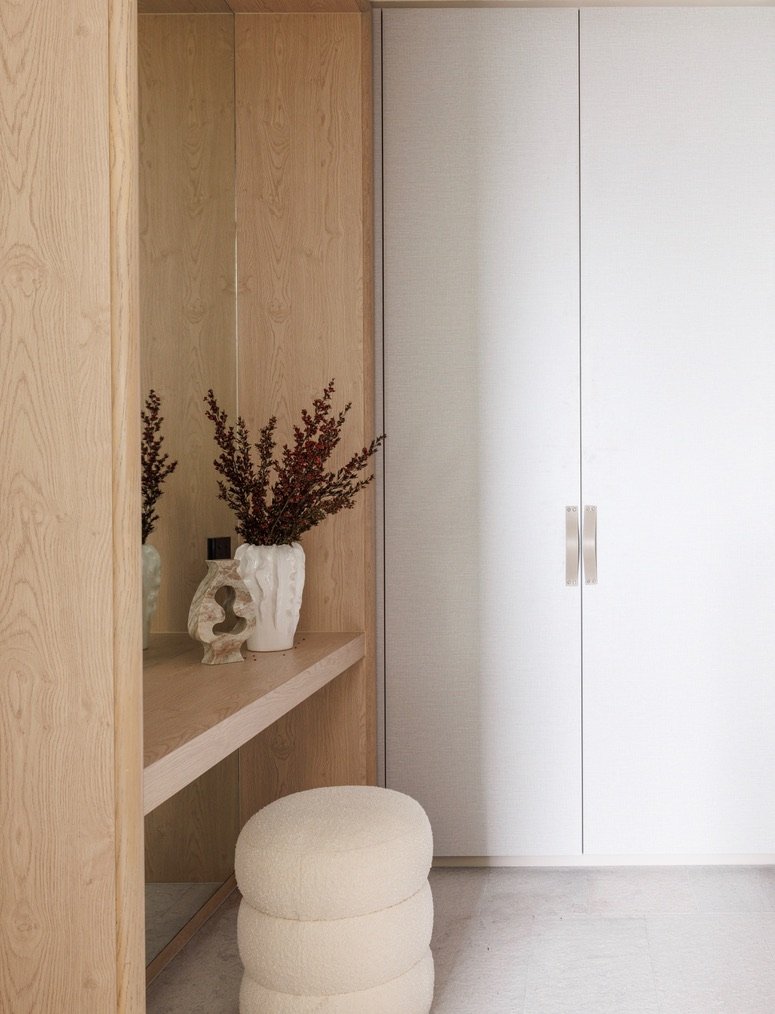 baptist street walk in robe featuring a wooden shelf with decorative vases and dried plants, a white pouf, and white closet doors.