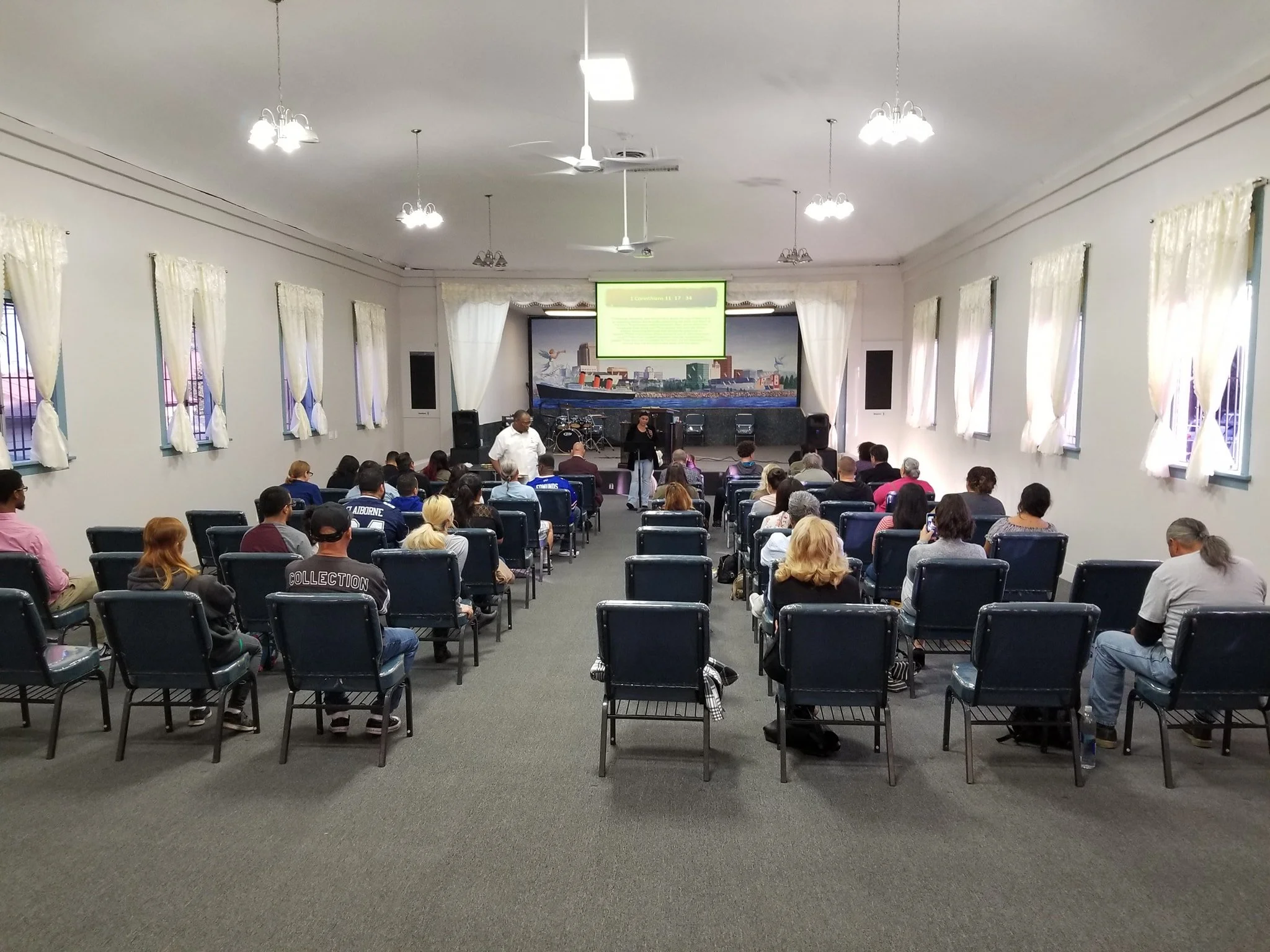 Iglesia de conferencias con asistentes escuchando una presentación en una pantalla grande y un escenario al frente.