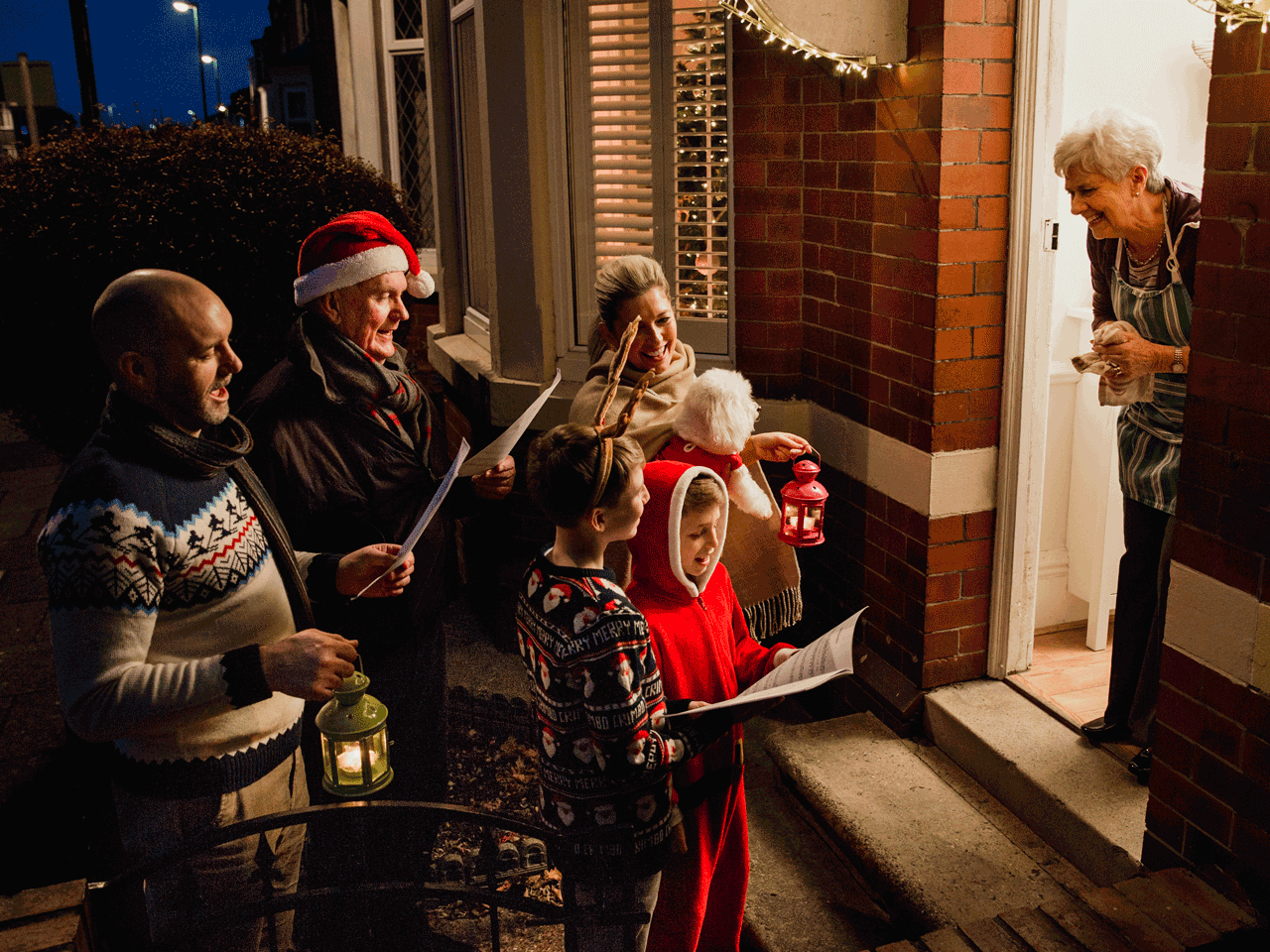 Familia en Halloween repartiendo dulces a una abuela en la puerta de su casa, decorada con luces navideñas y disfraces navideños.