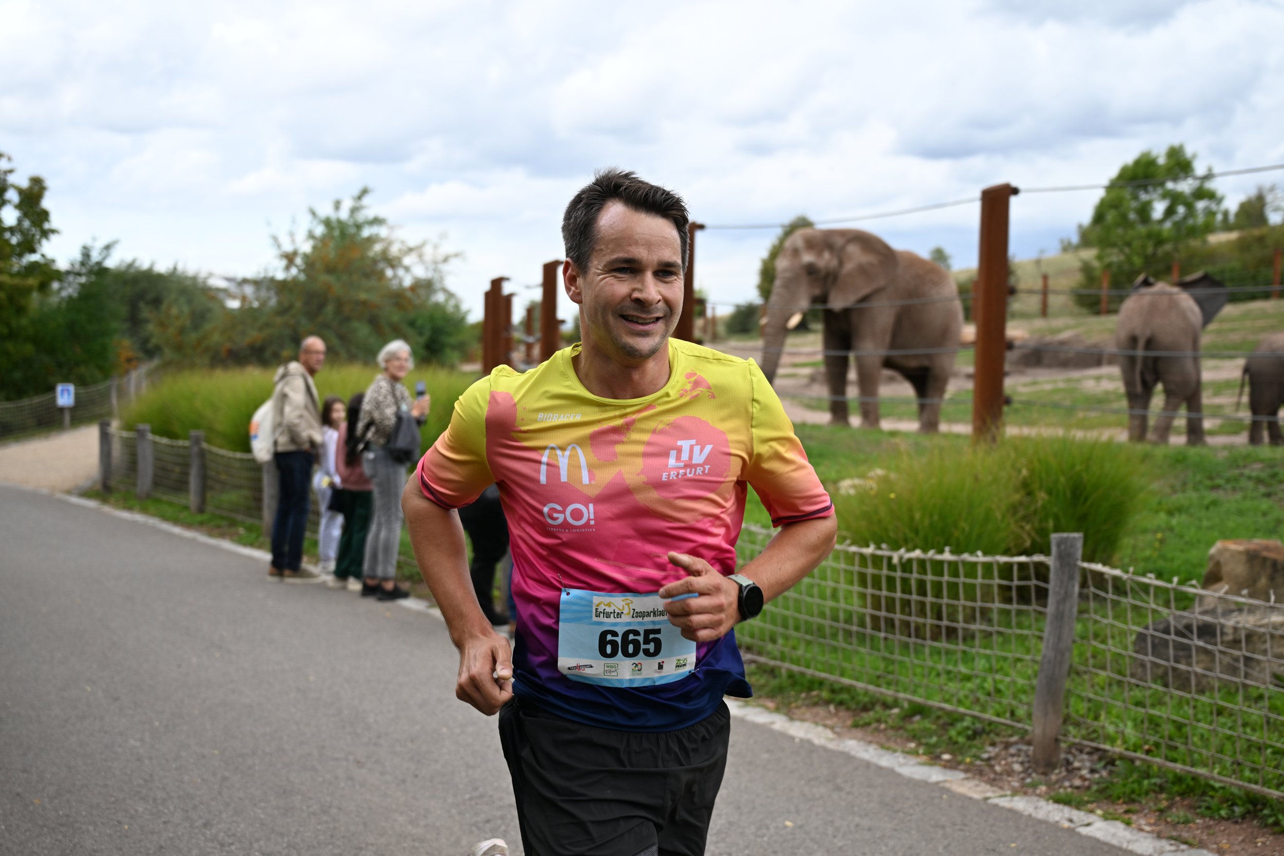 Läufer beim Marathon, im Hintergrund Tiere im Zoo, Zuschauer entlang der Strecke