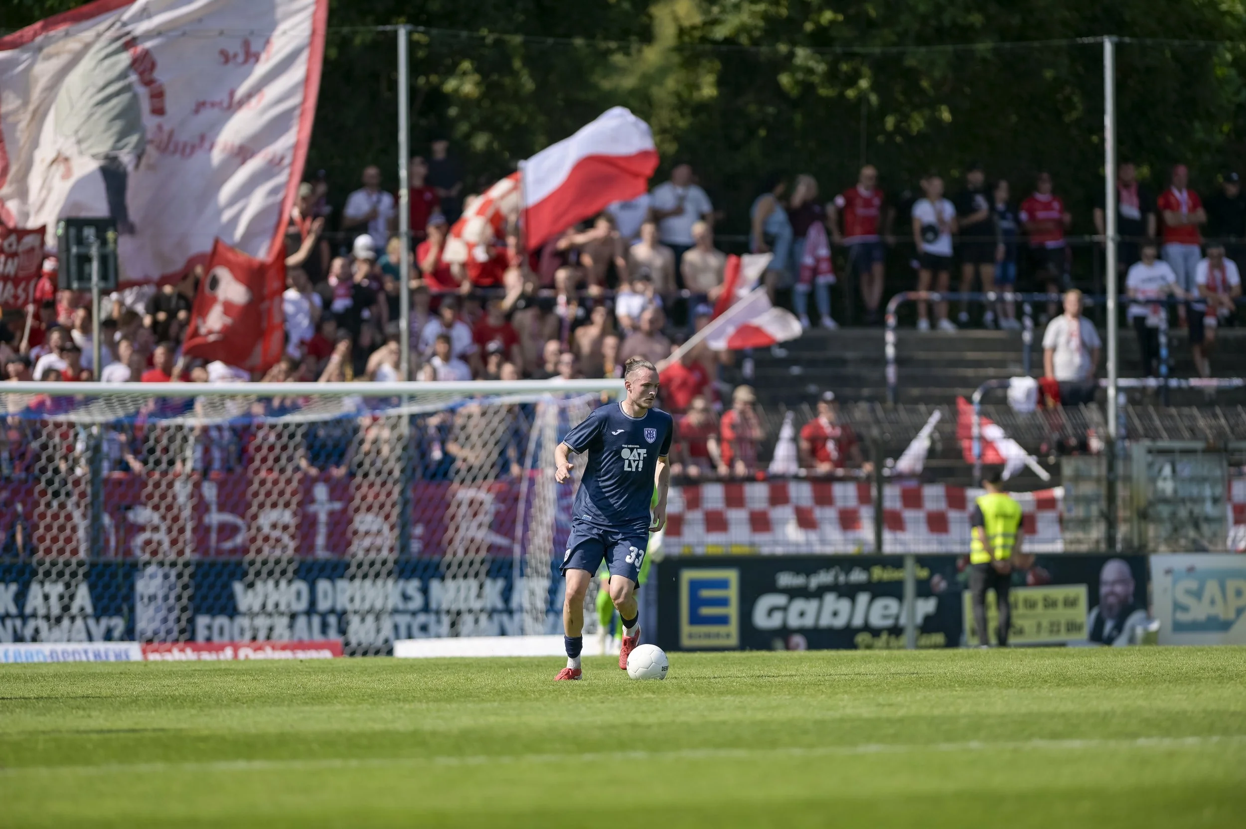Fußballspieler auf dem Spielfeld vor Fans in der Stadiontribüne, mit Fahnen im Hintergrund.