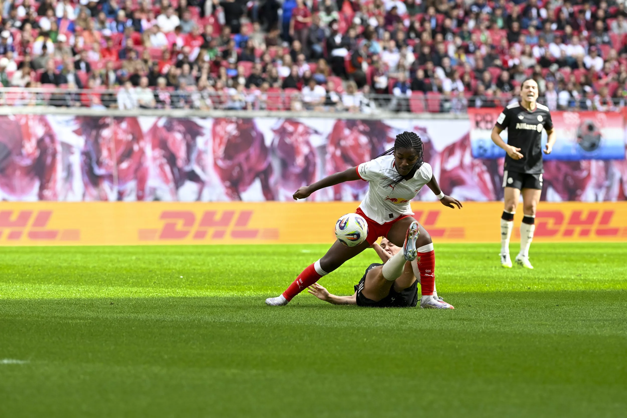 Fußballspiel mit zwei Spielern, eine liegt am Boden, die andere steht, vor einer großen Zuschauermenge
