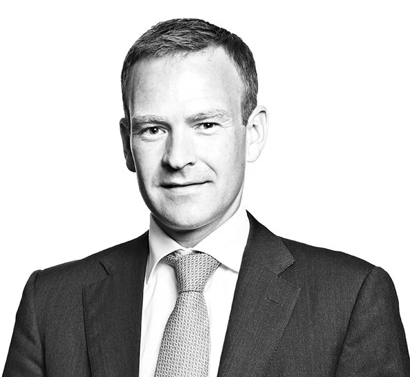 Black and white professional portrait of a man in a suit and tie, with short hair, facing forward.