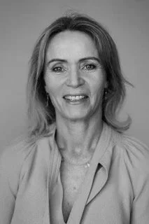 Smiling woman with blonde hair, wearing a light blue blouse, facing forward against a plain background.