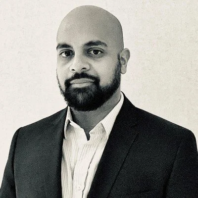 A black and white professional portrait of a man in a suit and collared shirt with a bald head and beard.