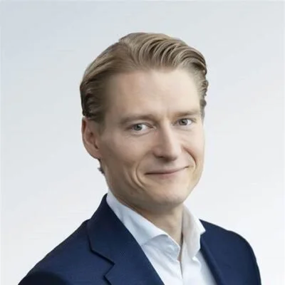 A professional headshot of a smiling man in a suit and tie against a textured blue background.