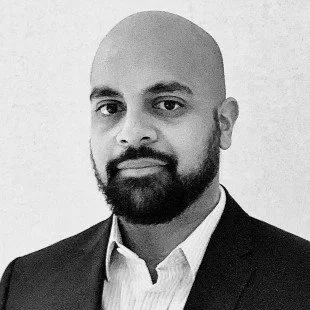 A black and white professional portrait of a man in a suit and collared shirt with a bald head and beard.