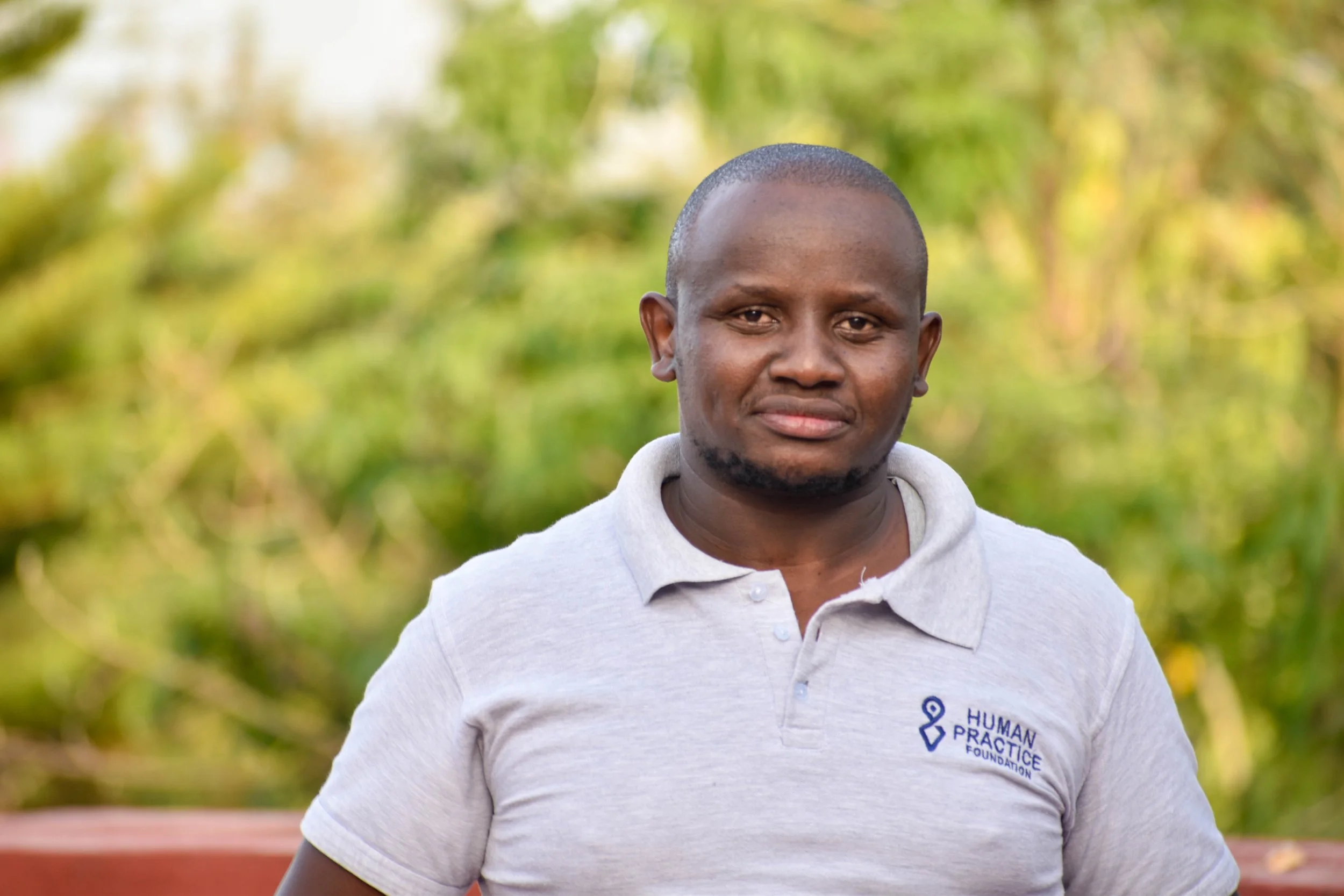 A professional headshot of a smiling man in a suit and tie against a textured blue background.