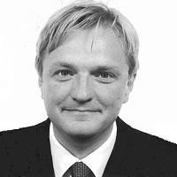 Black and white headshot of a man with light hair, wearing a suit and tie, smiling slightly.
