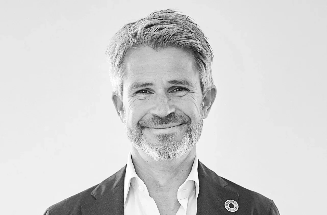 Black and white portrait of a middle-aged man with gray hair and beard, wearing a suit and white shirt, smiling, against a plain background.