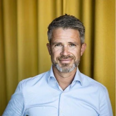 Black and white portrait of a middle-aged man with gray hair and beard, wearing a suit and white shirt, smiling, against a plain background.
