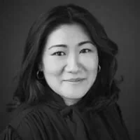 Portrait of an Asian woman with shoulder-length black hair, wearing a dark blouse, smiling lightly against a neutral background.