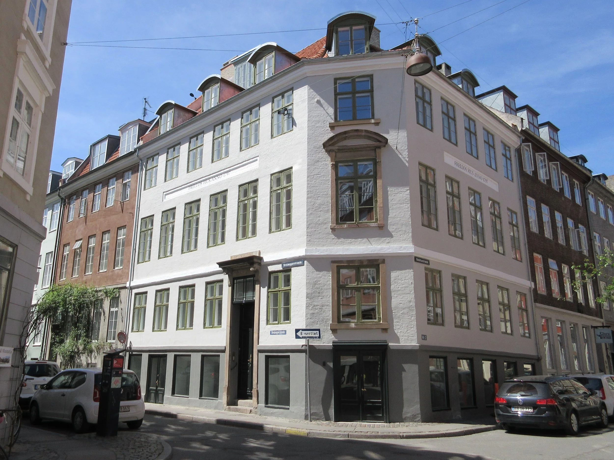 A white corner building with multiple windows, located on a city street with parked cars.