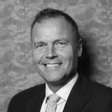Professional portrait of a man wearing a suit and a tie, smiling against a blue textured background.