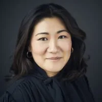 Portrait of an Asian woman with shoulder-length black hair, wearing a dark blouse, smiling lightly against a neutral background.