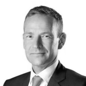 Black and white professional portrait of a man in a suit and tie, with short hair, facing forward.