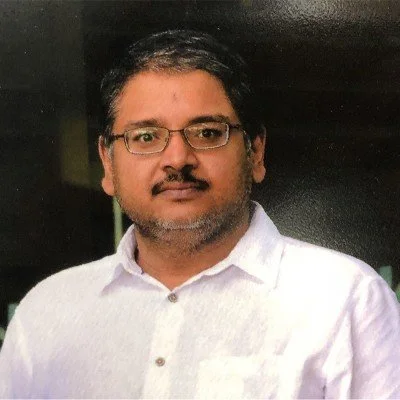 A man with glasses, dark hair, and a beard wearing a white shirt.