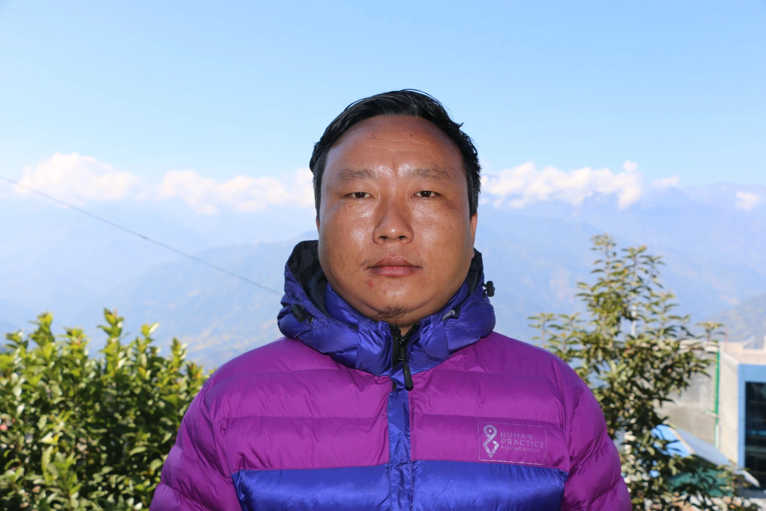 A professional headshot of a smiling man in a suit and tie against a textured blue background.