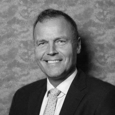 A professional headshot of a smiling man in a suit and tie against a textured blue background.