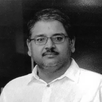 A man with glasses, dark hair, and a beard wearing a white shirt.
