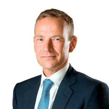 Black and white professional portrait of a man in a suit and tie, with short hair, facing forward.