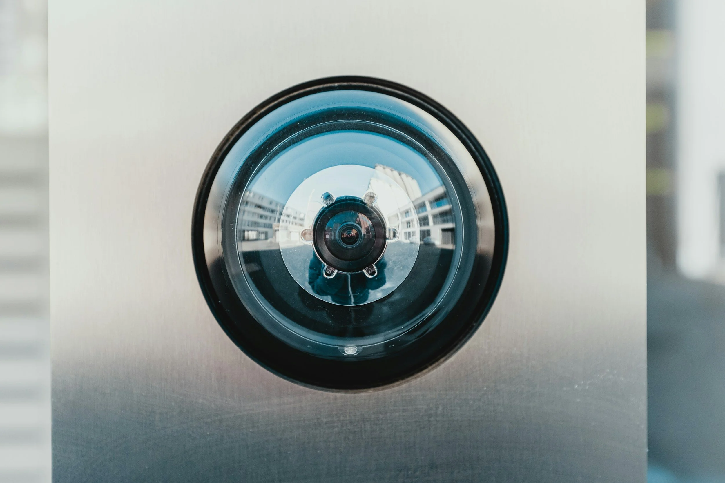 Close-up of a modern security camera mounted on a building, with a cityscape and an apartment complex reflected in its lens.