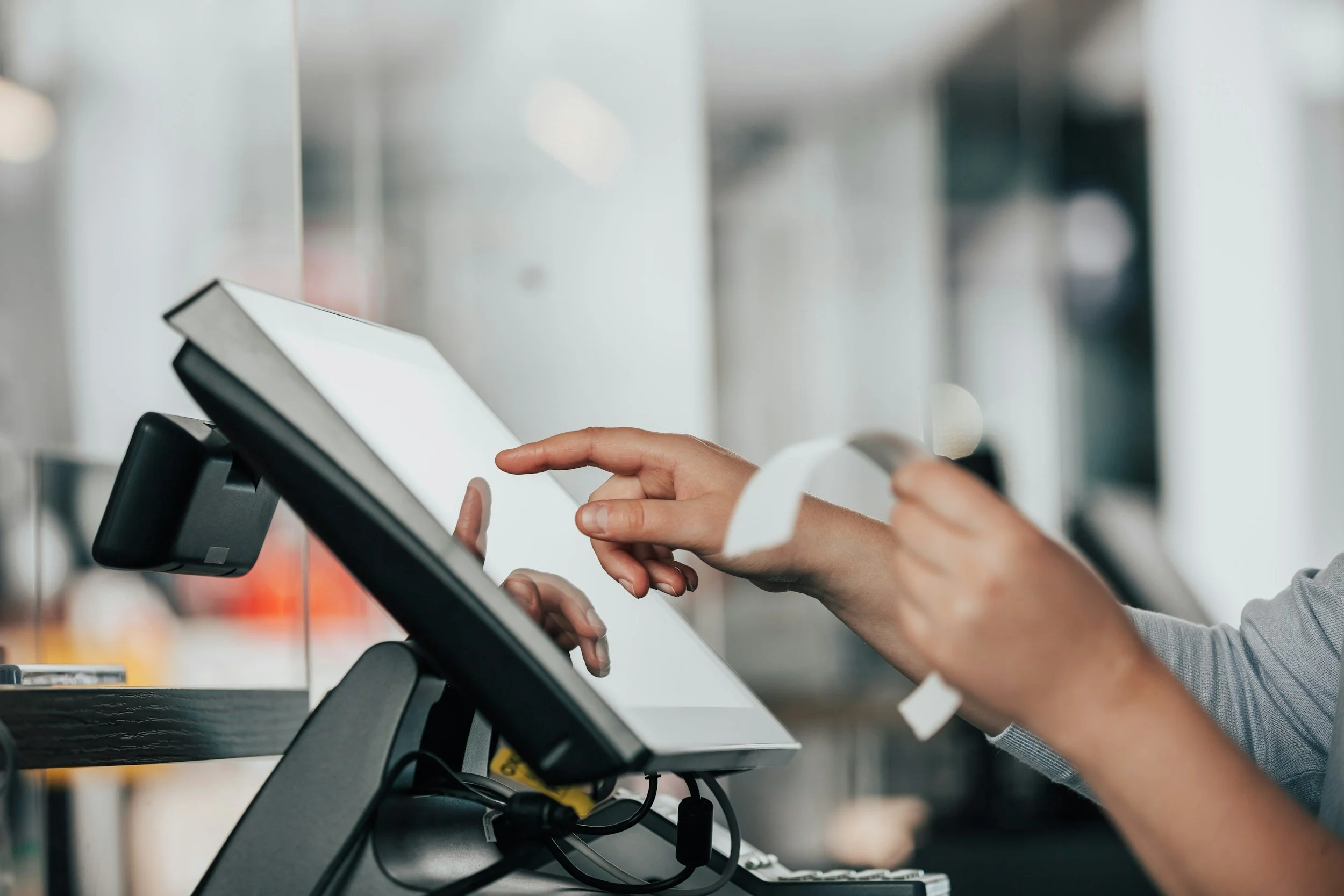 Person using a touch screen checkout register at a store, with a hand holding a credit or debit card.