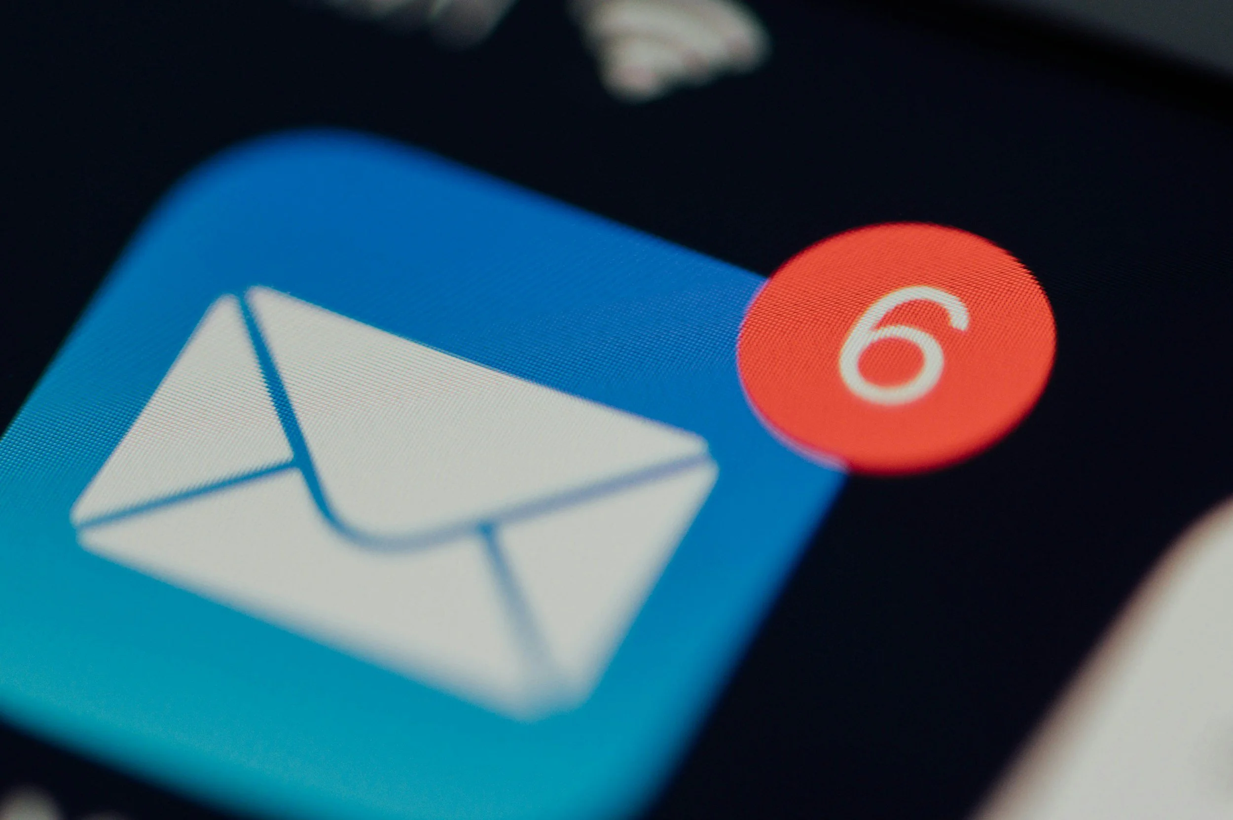 Close-up of a digital device screen showing an app icon with a white envelope on a blue background and a notification bubble with the number 6 in white on a red background.