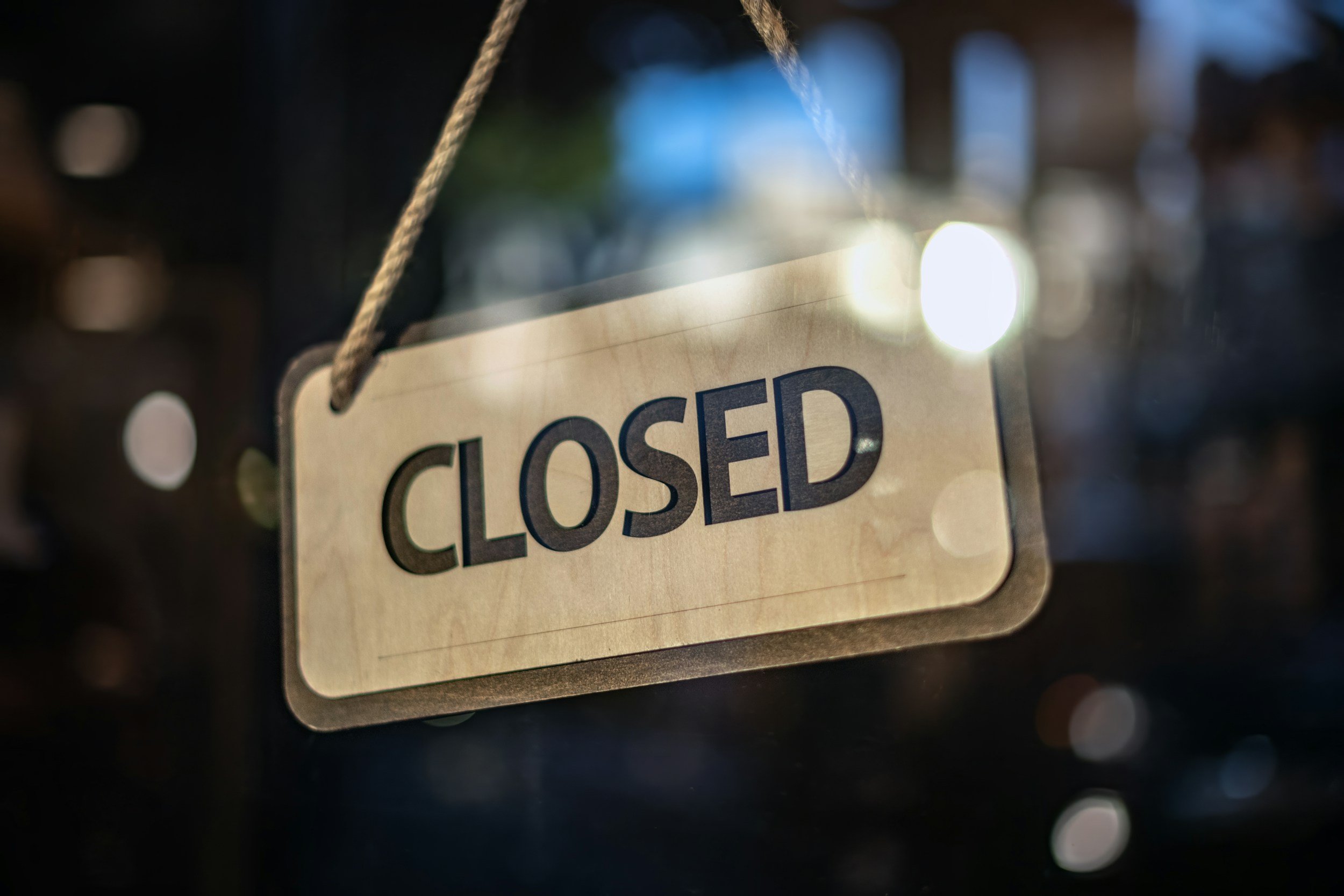 Close-up of a 'CLOSED' sign hanging on a dark background with bokeh lights.