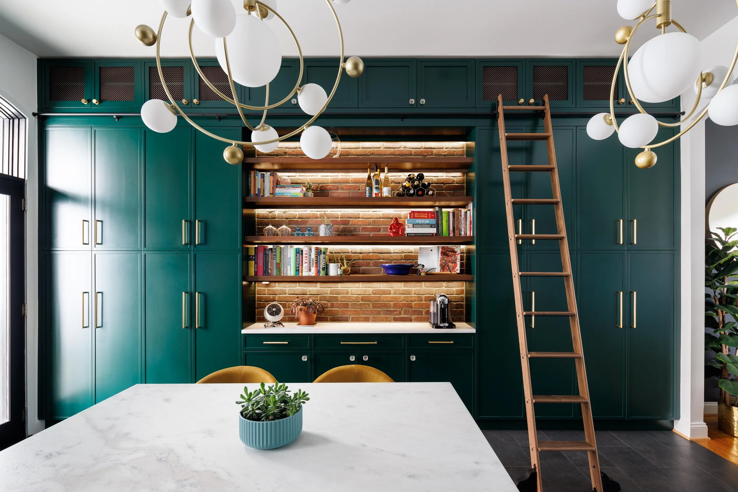 I helped transform a cramped, walled‑off kitchen and dining room into a unified, social hub complete with an island, breakfast bar, and dry bar. Bold, emerald floor‑to‑ceiling cabinetry—offset by stained walnut floating shelves and exposed brick—maxi