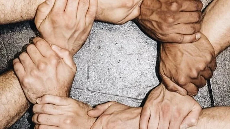 Six hands of different skin tones are clasped together forming a circle on a dark floor.