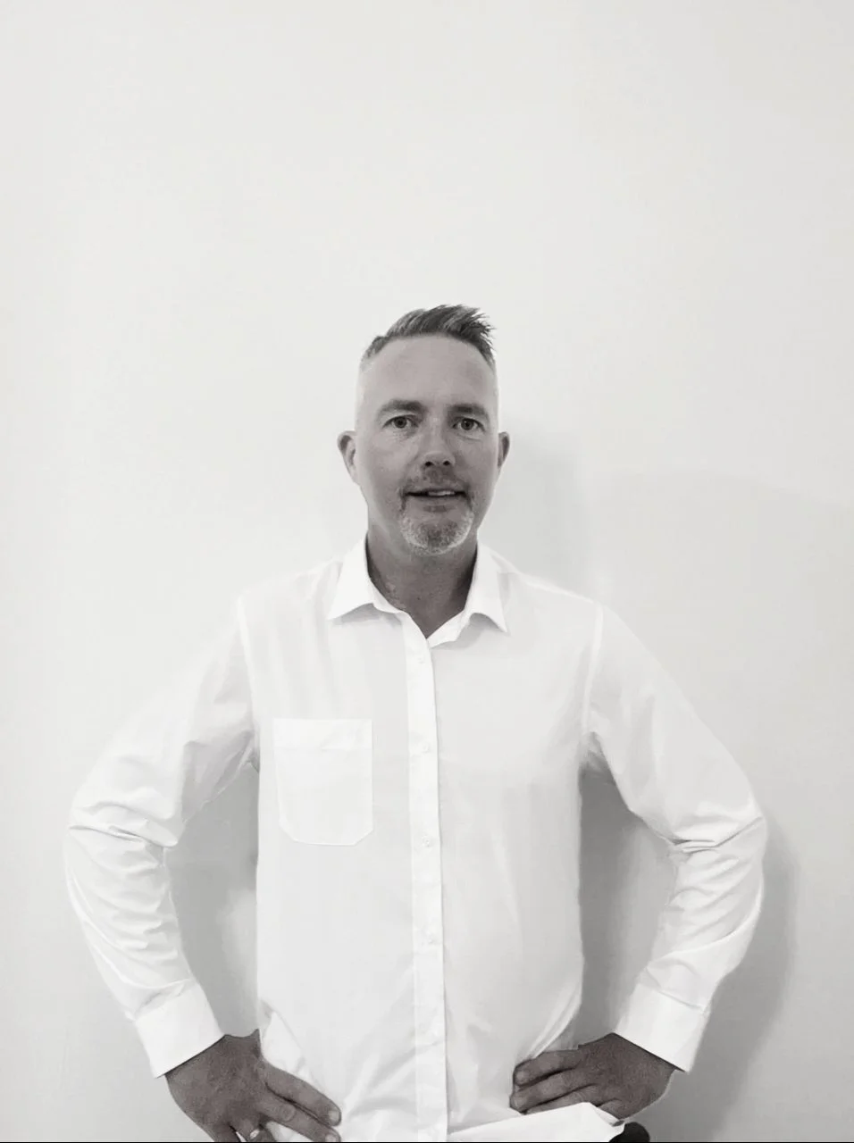 Black and white portrait of contemporary artist and printmaker Mark James Murphy in a white shirt, standing against a neutral background in his Vũng Tàu studio.