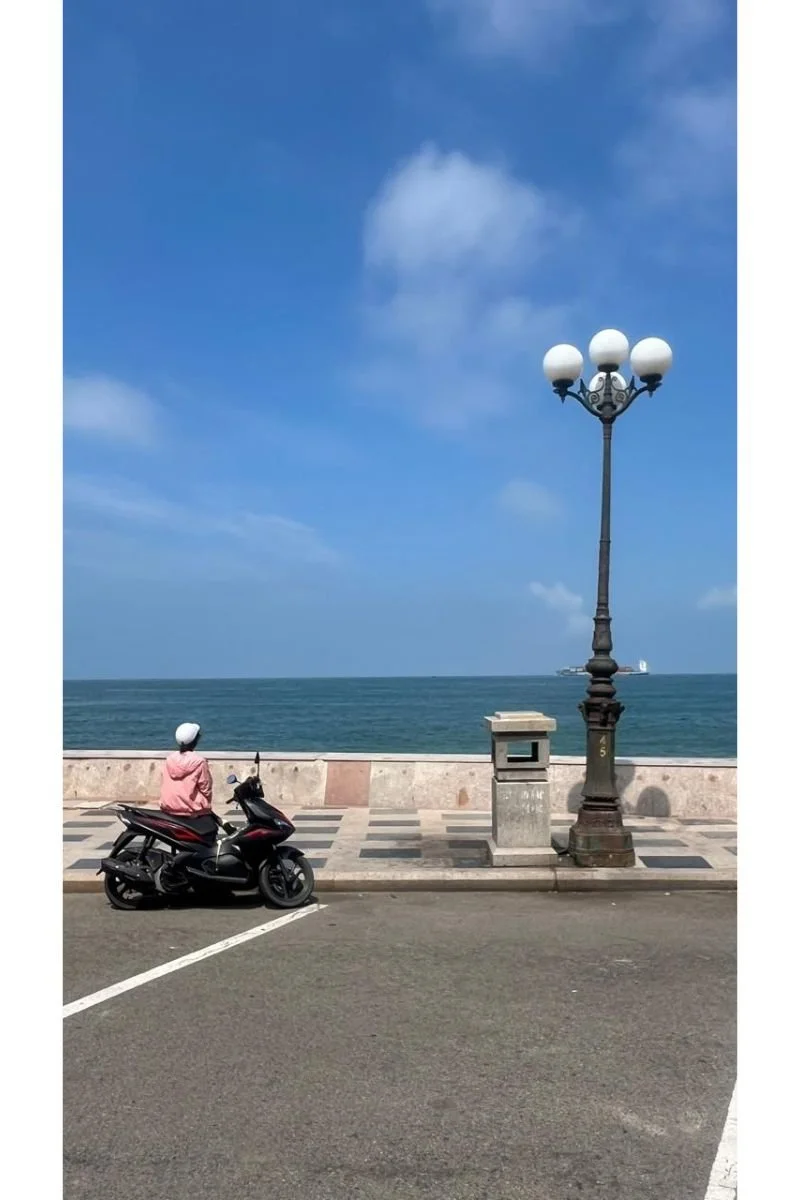 woman leaning against motorbike scooter looking out at sea in Vung Tau Vietnam