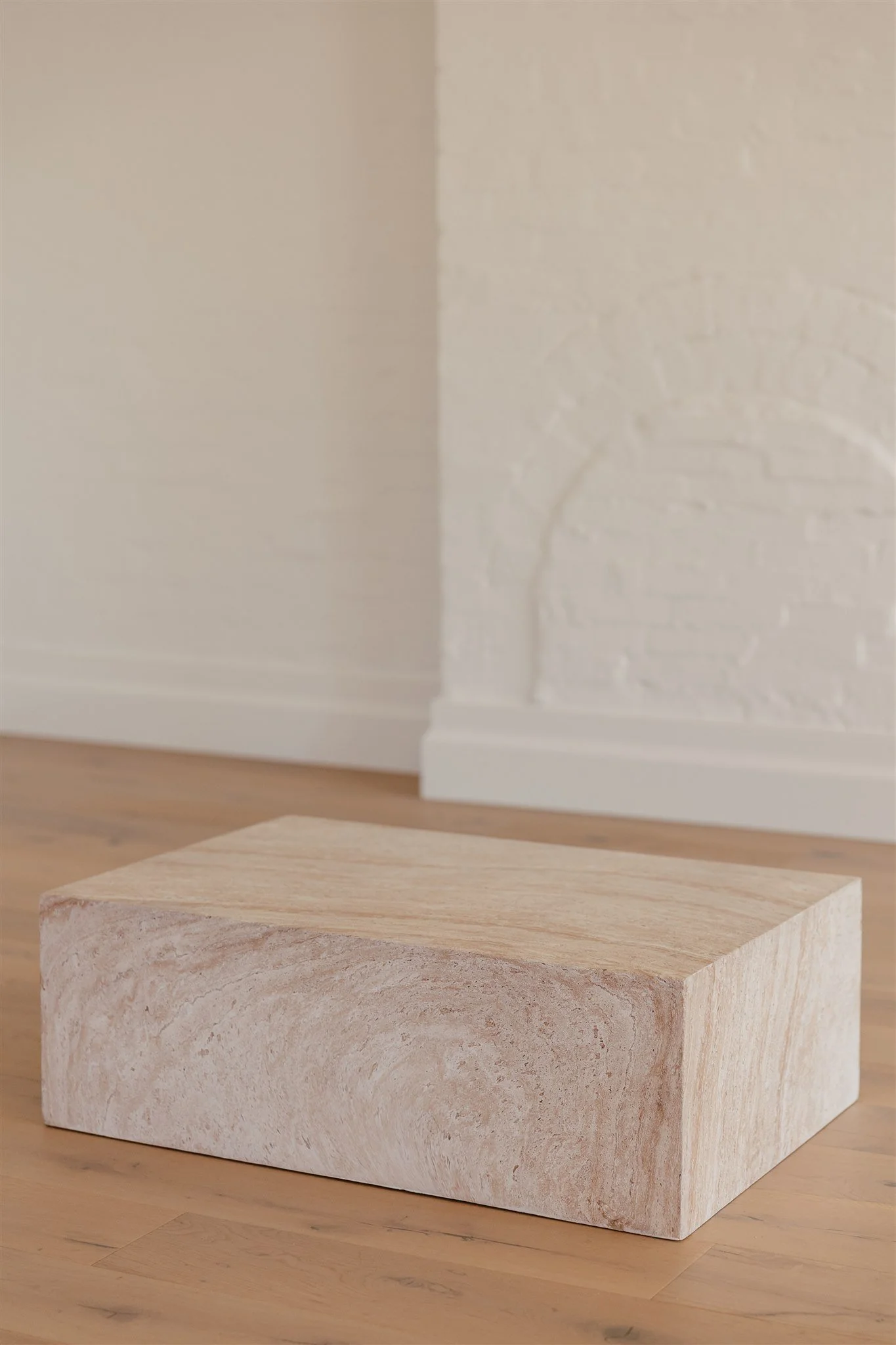 A rectangular, natural stone block on a wooden floor near a white wall with brick texture.