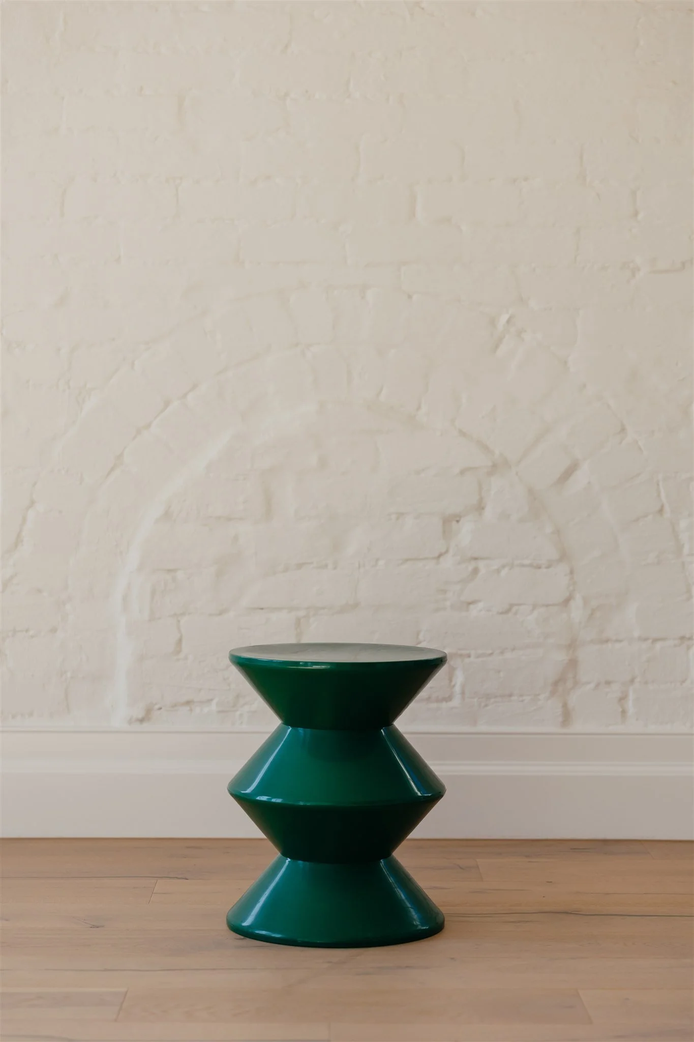 A modern, green, geometric side table against a white brick wall with an arch detail.