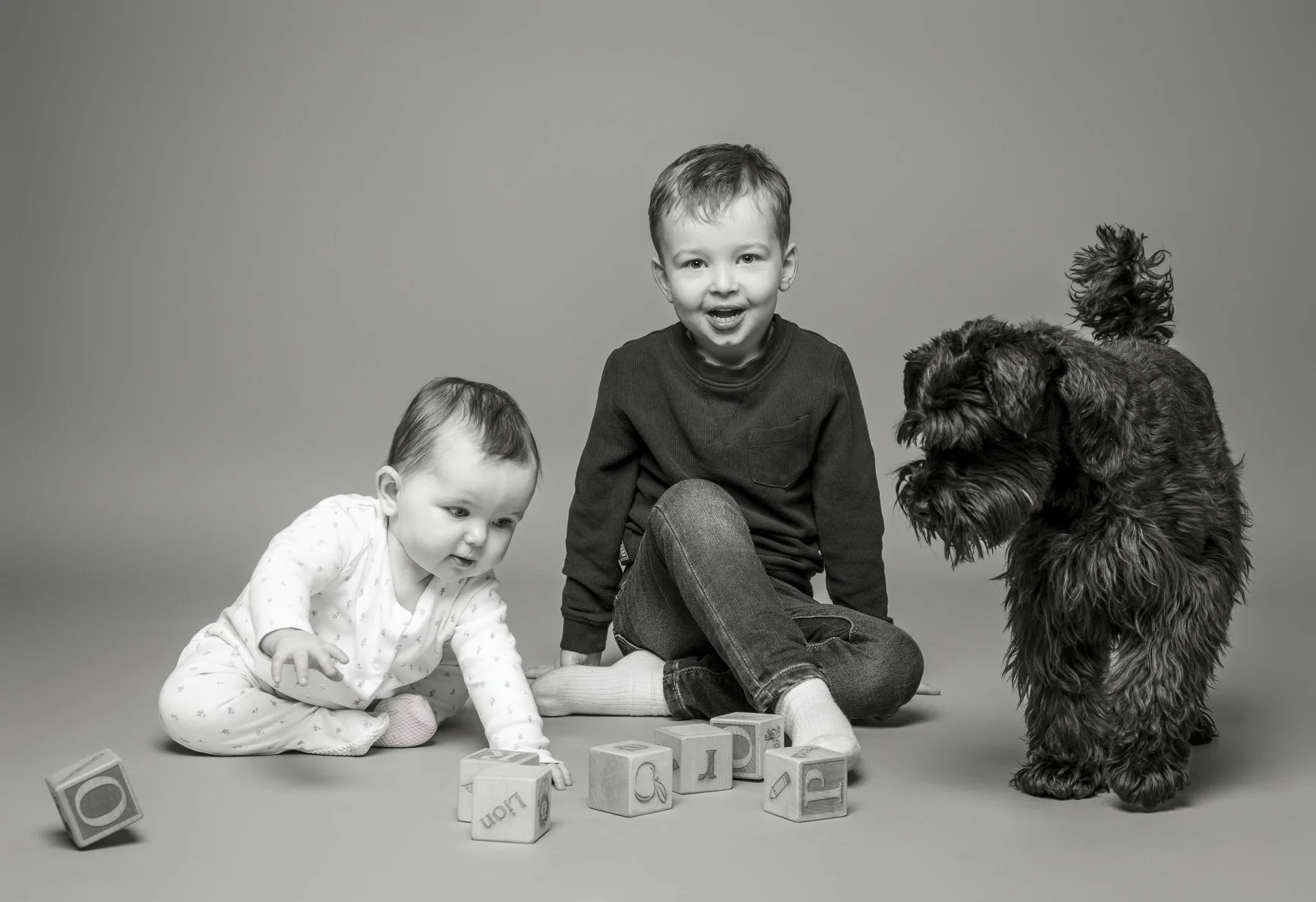 Black and white studio portrait of a baby playing with blocks, captured by Artis Studios