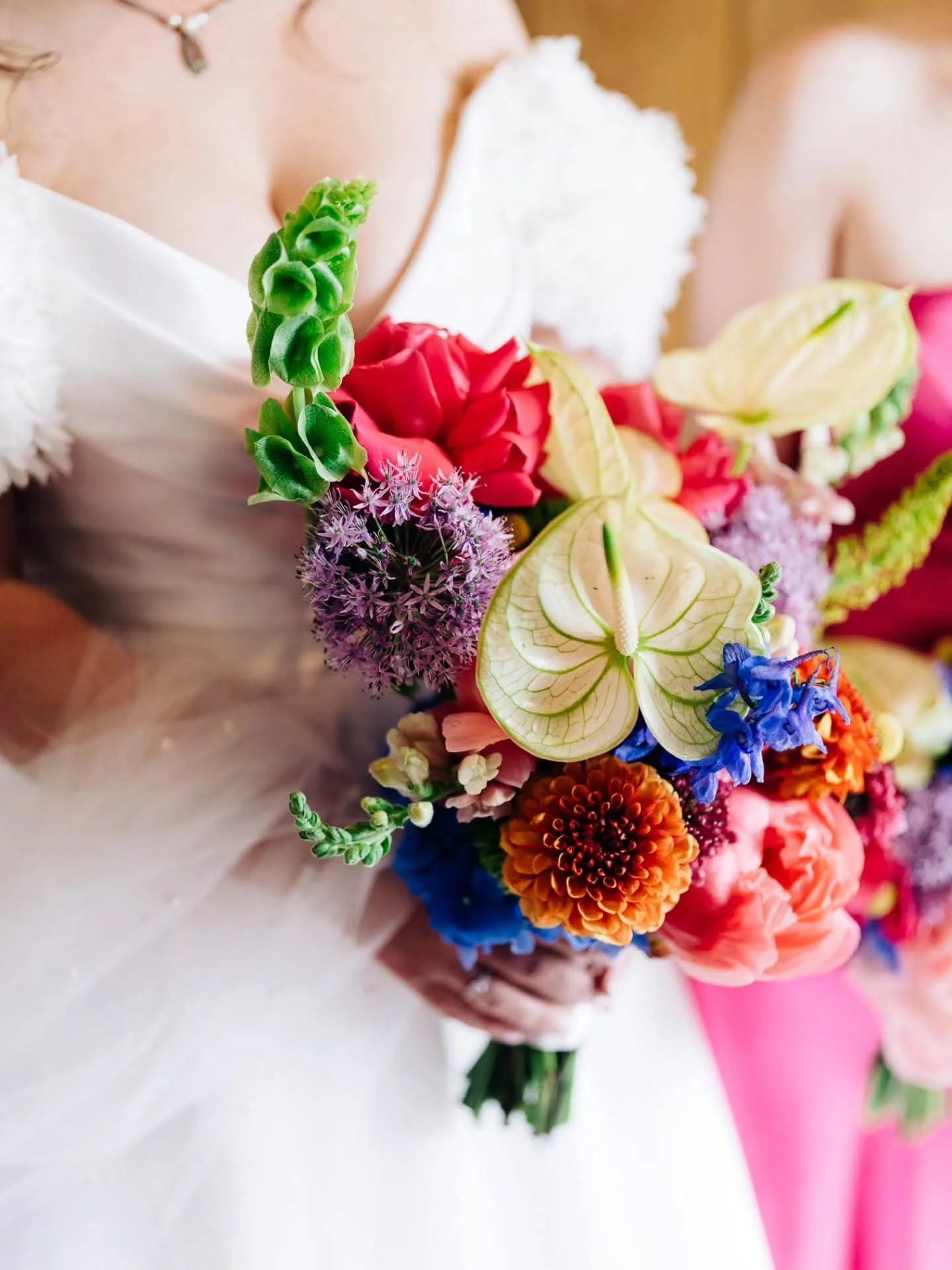 Close-up of a colorful flower bouquet with pink, orange, yellow, purple, and blue flowers, wrapped in pink and white paper.