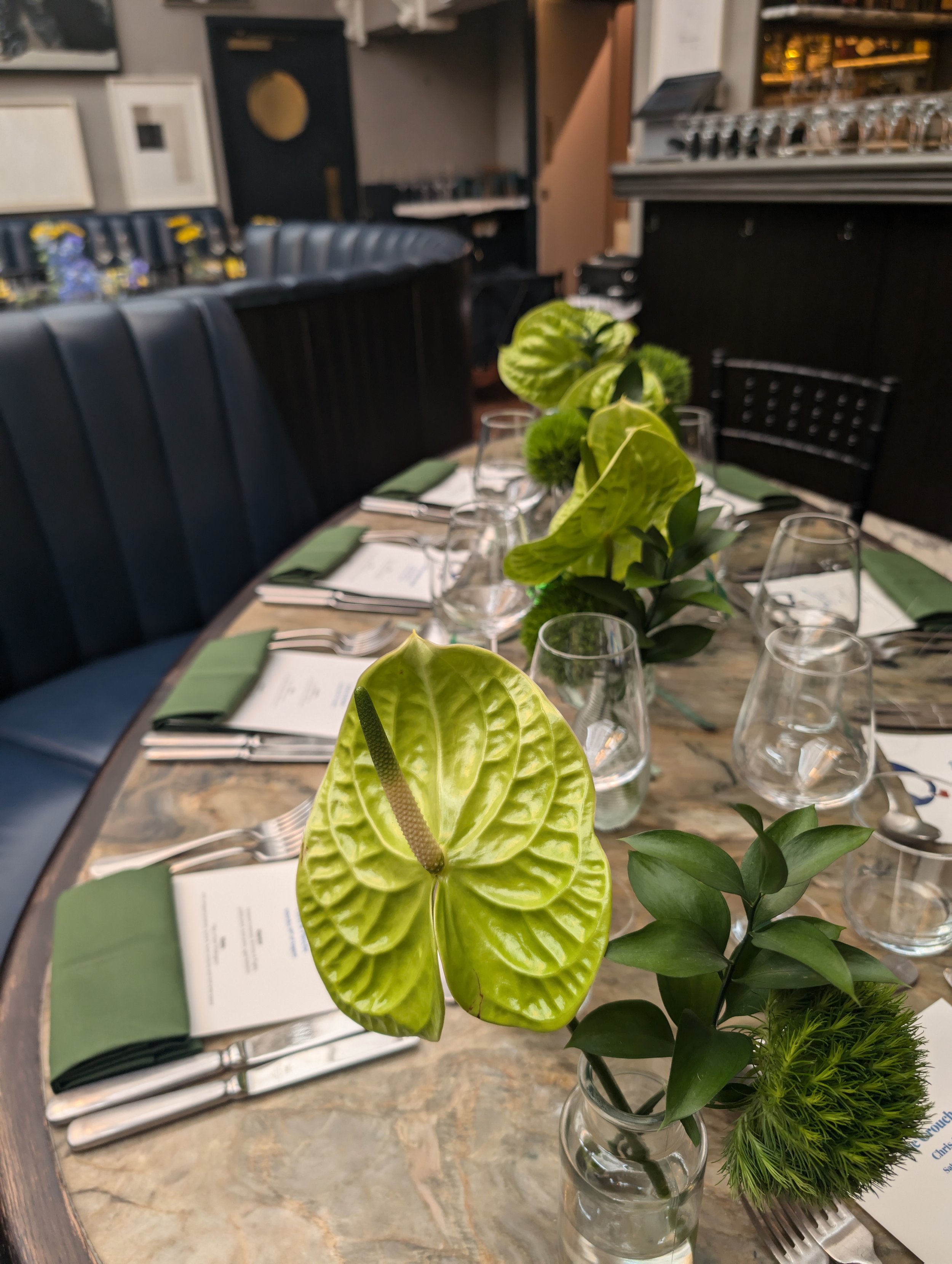 A dining table decorated with green plants, wine glasses, and menus in a restaurant setting.