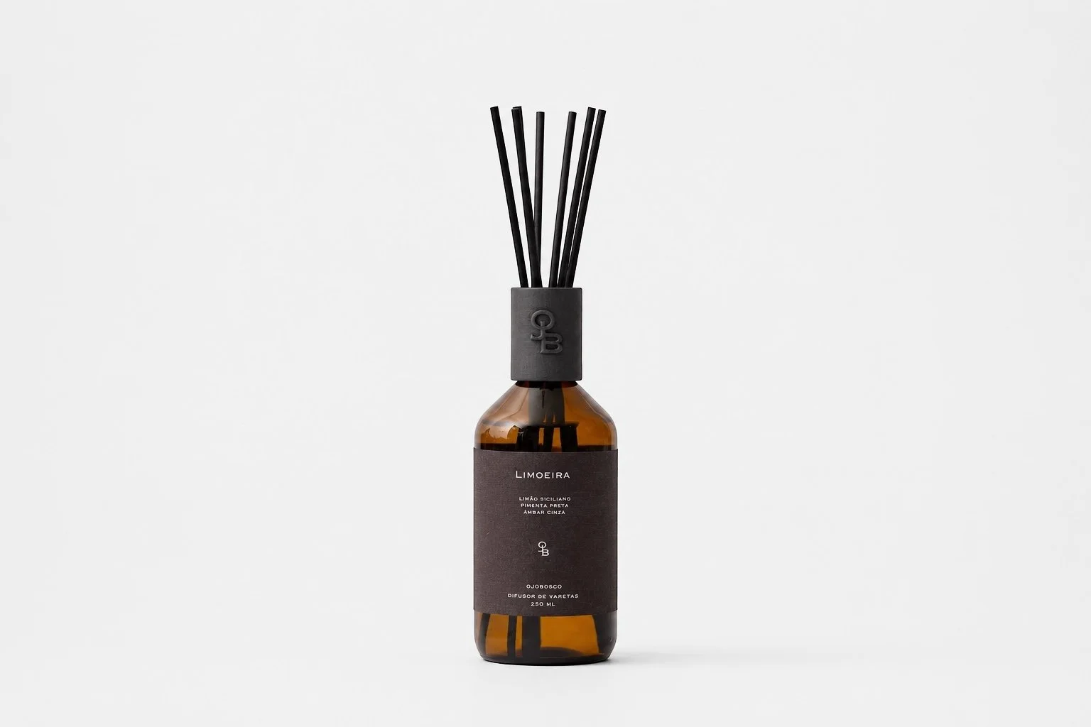 Frasco de vidro âmbar com etiqueta preta, contendo difusor de aromas com varetas pretas, sobre fundo branco.