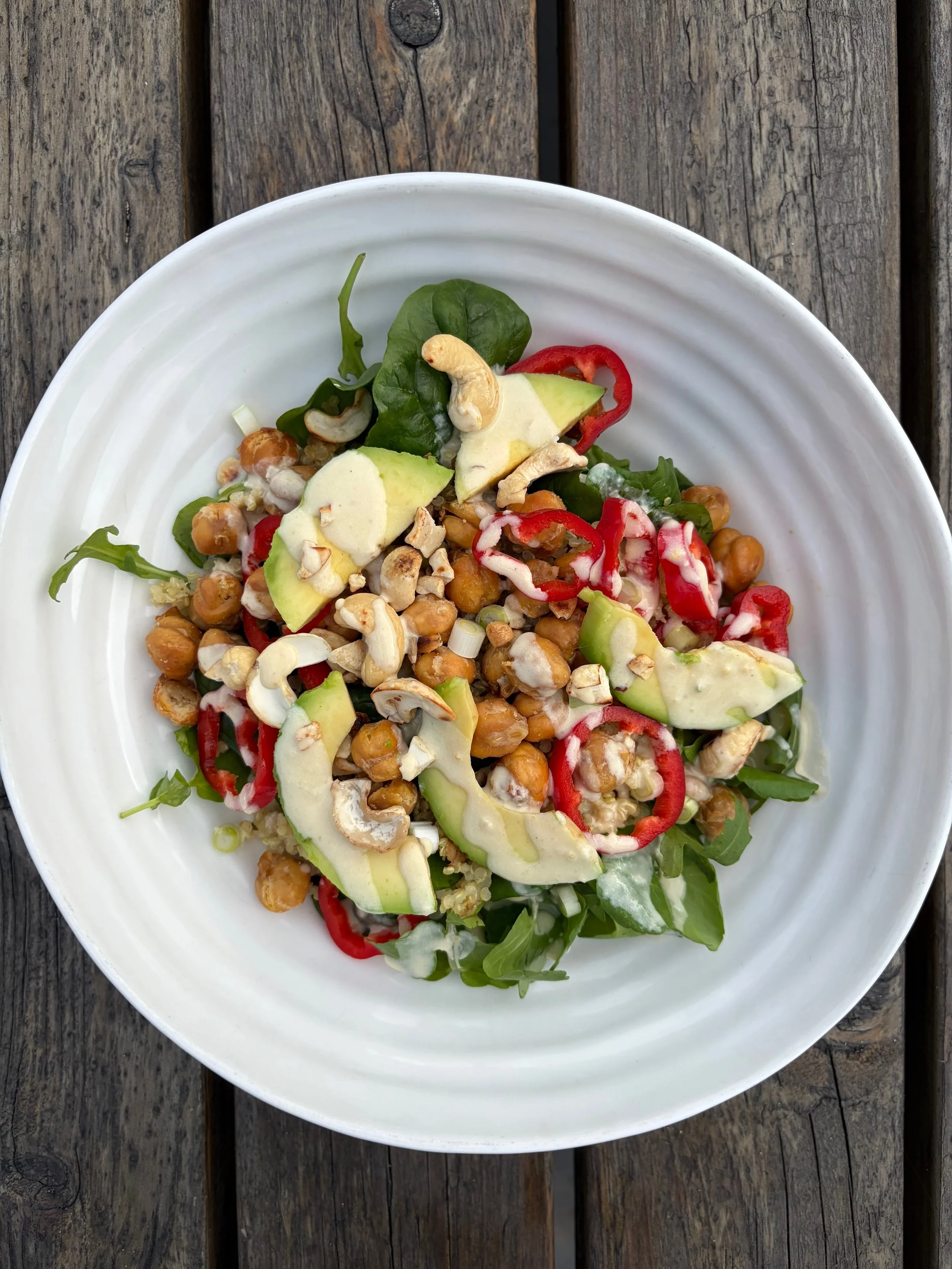 White ridged bowl with avocado, chickpeas, red pepper, cashew nuts, green leaves and a creamy dressing